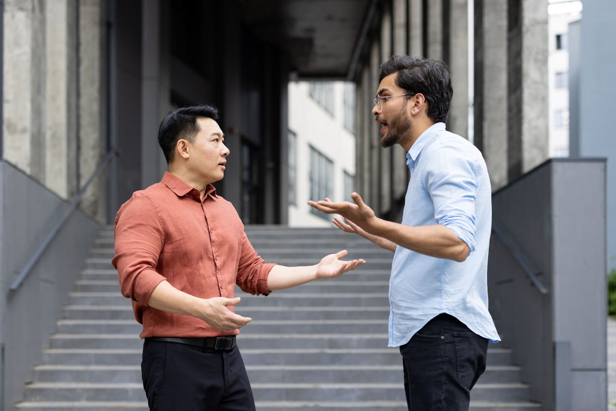 An intense exchange between two colleagues on office stairs captures a moment of workplace conflict. The image reflects emotions such as anger and stress, highlighting professional disagreements.