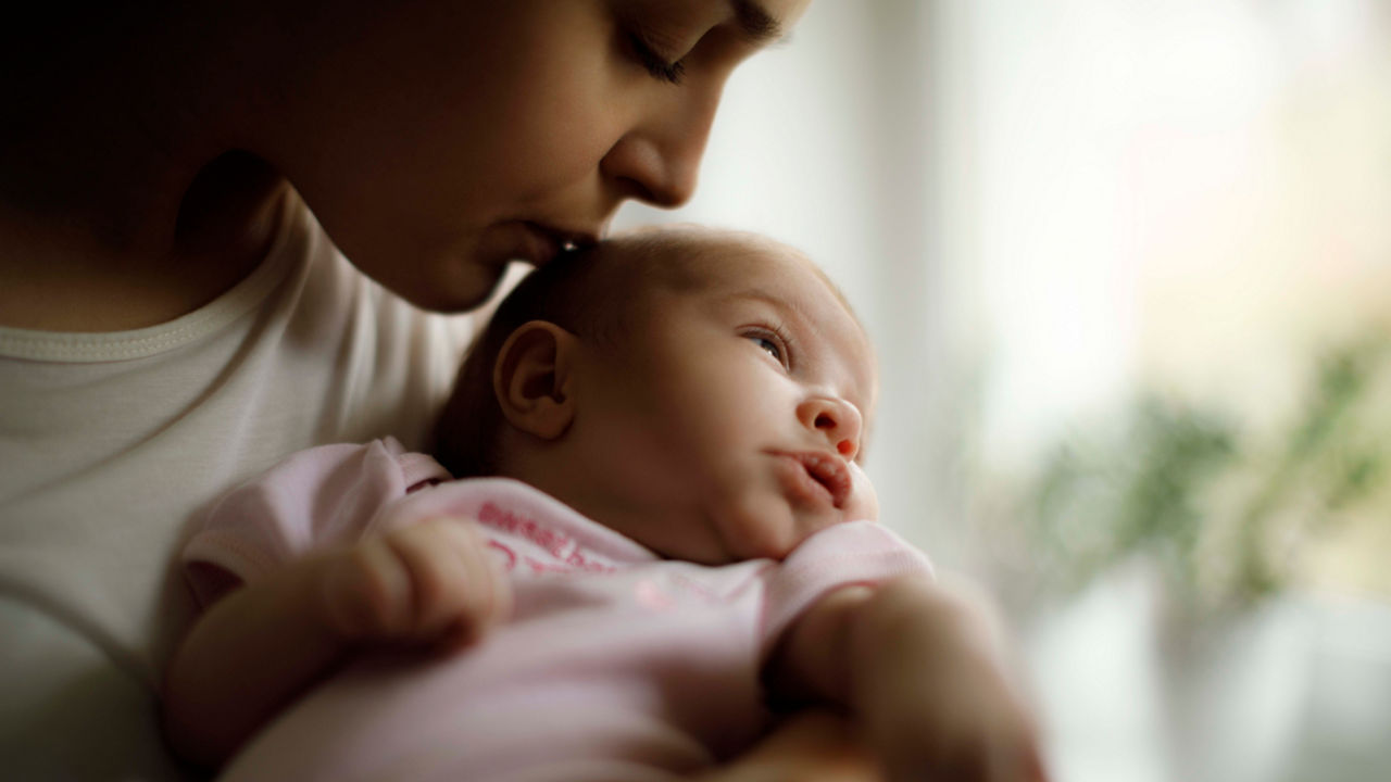 A woman kisses her baby in front of a window.