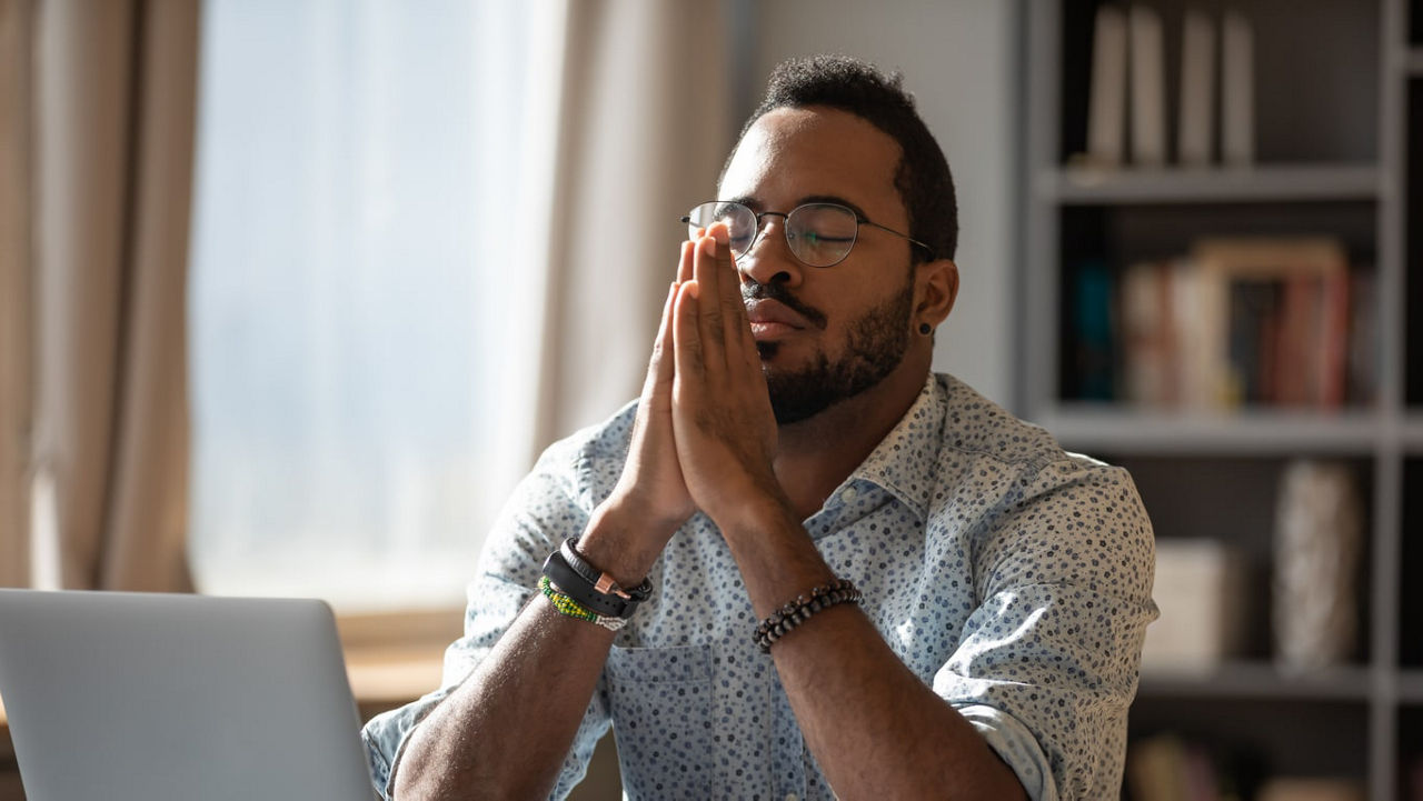 A man praying while working on his laptop.