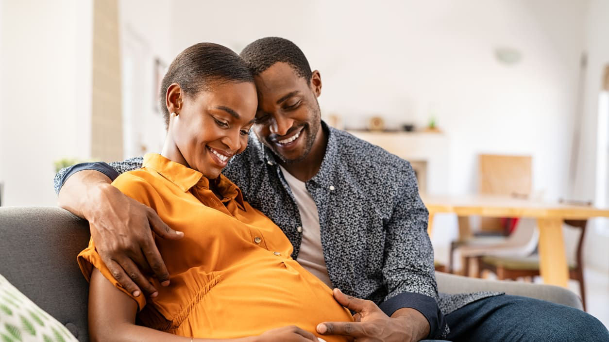 A pregnant woman and her husband are sitting on a couch.