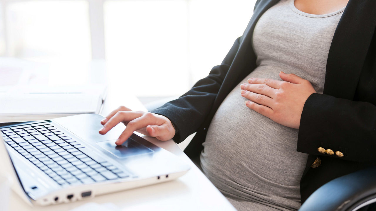 A pregnant woman working on a laptop.
