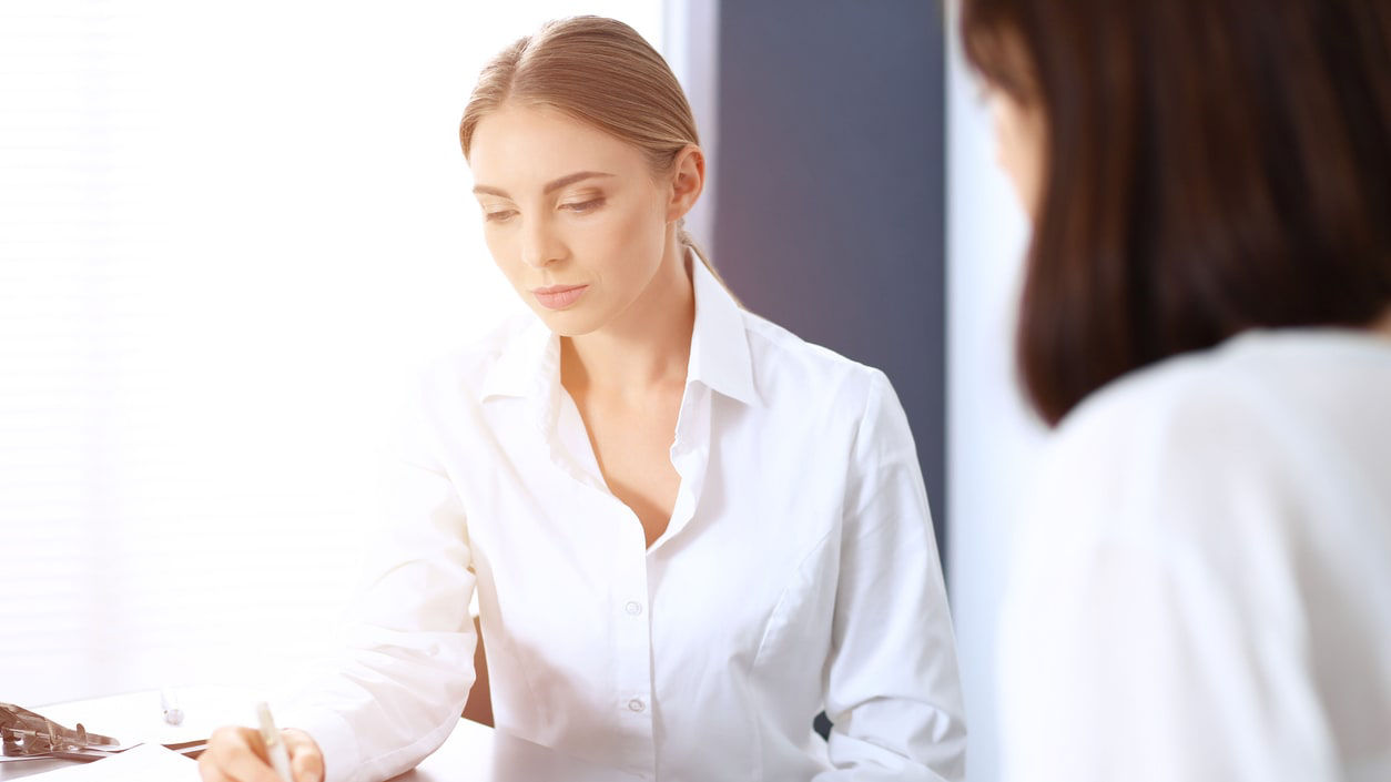  A woman diligently writes on a piece of paper, with a pen in hand, in a well-lit study area.