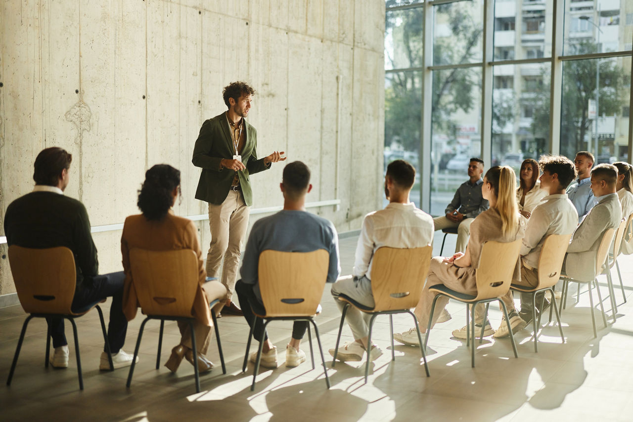 Young CEO talking to large group of his colleagues during an education event in the office. Copy space.