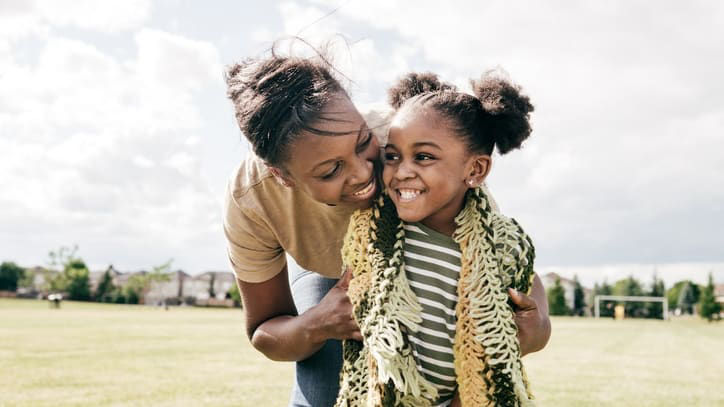 A mother and daughter hugging on a grassy field.