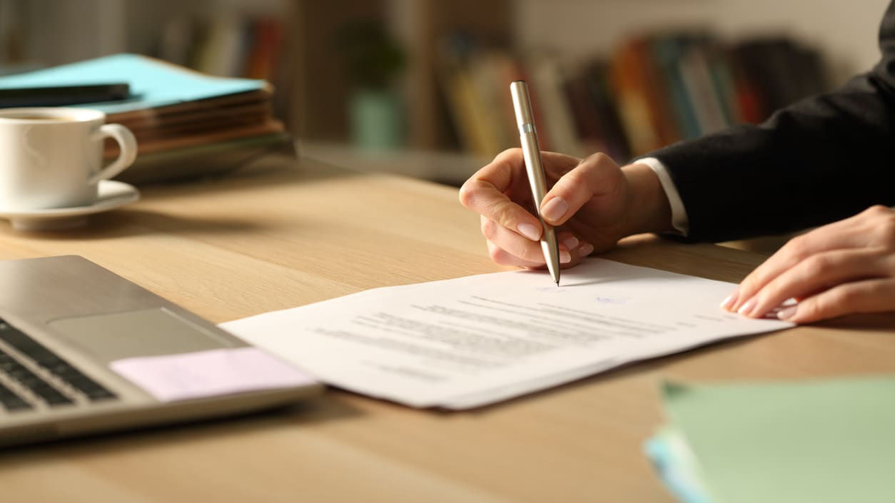 A person signing a document at a desk.