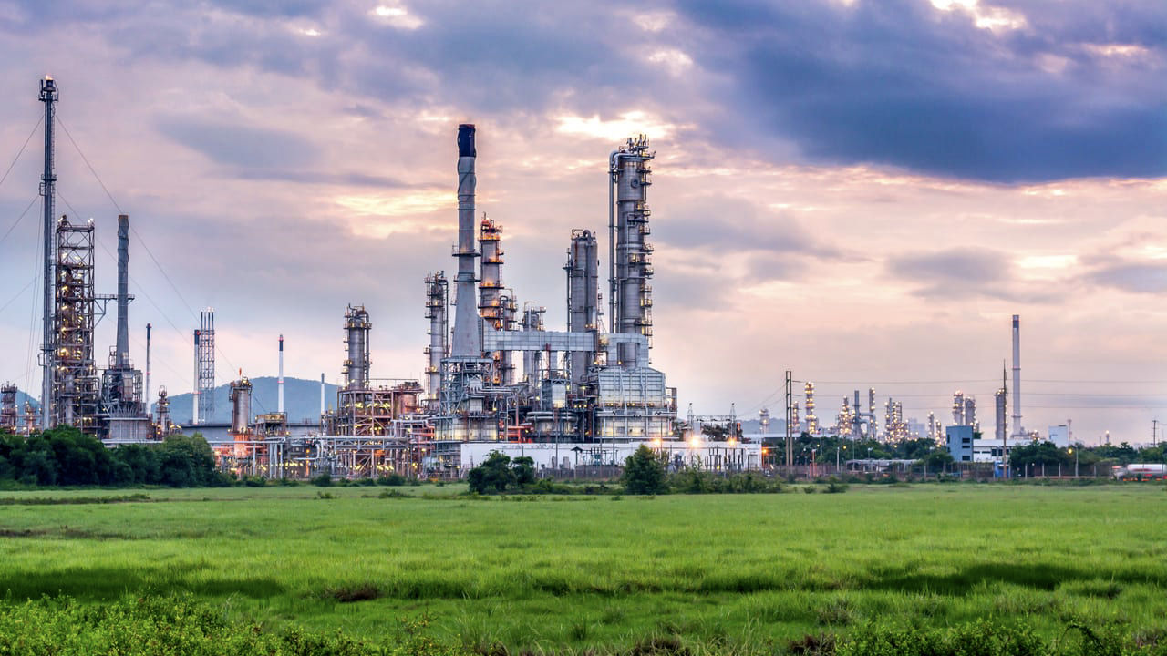 An oil refinery at dusk with clouds in the sky.