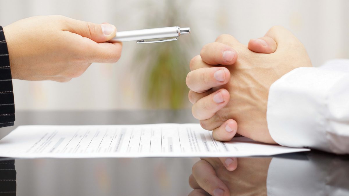 Someone refusing to sign a document, fingers crossed into a ball on the table.as someone else offers a pen.