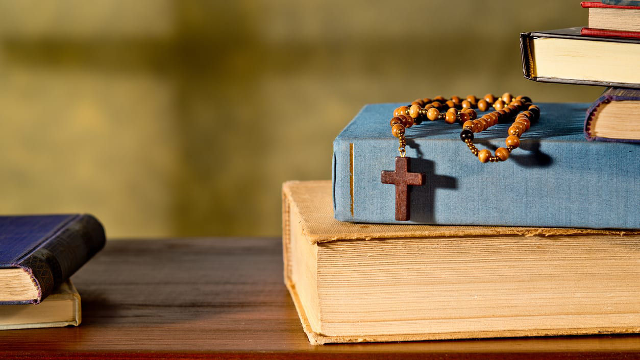 A wooden rosary sits on top of a stack of books.