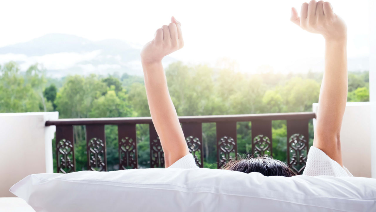 A woman is waking up in bed with her arms raised.