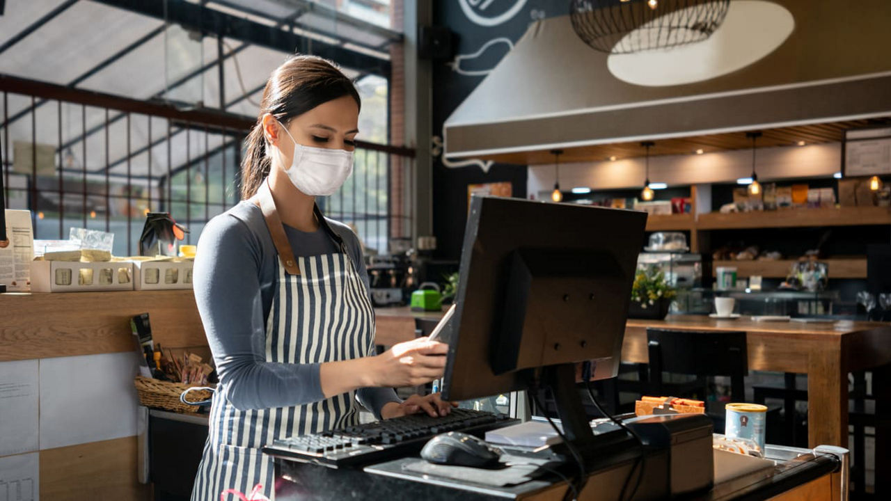 A woman wearing a face mask is working at a coffee shop.