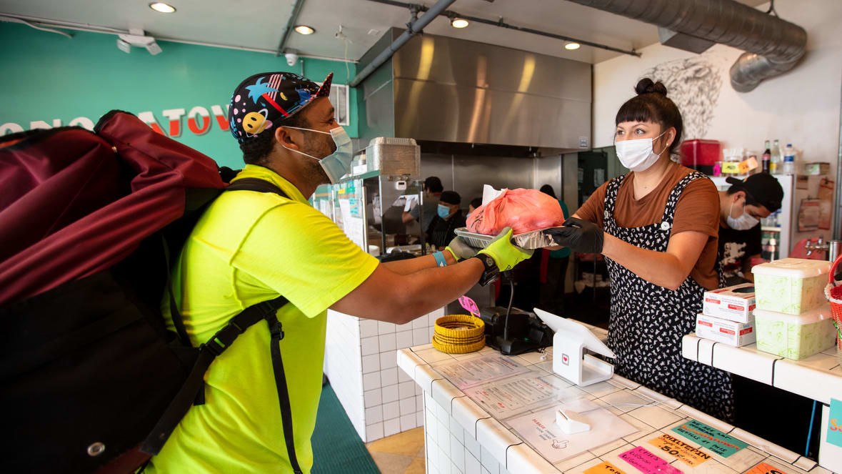 A woman wearing a face mask and carrying a bag at a counter.