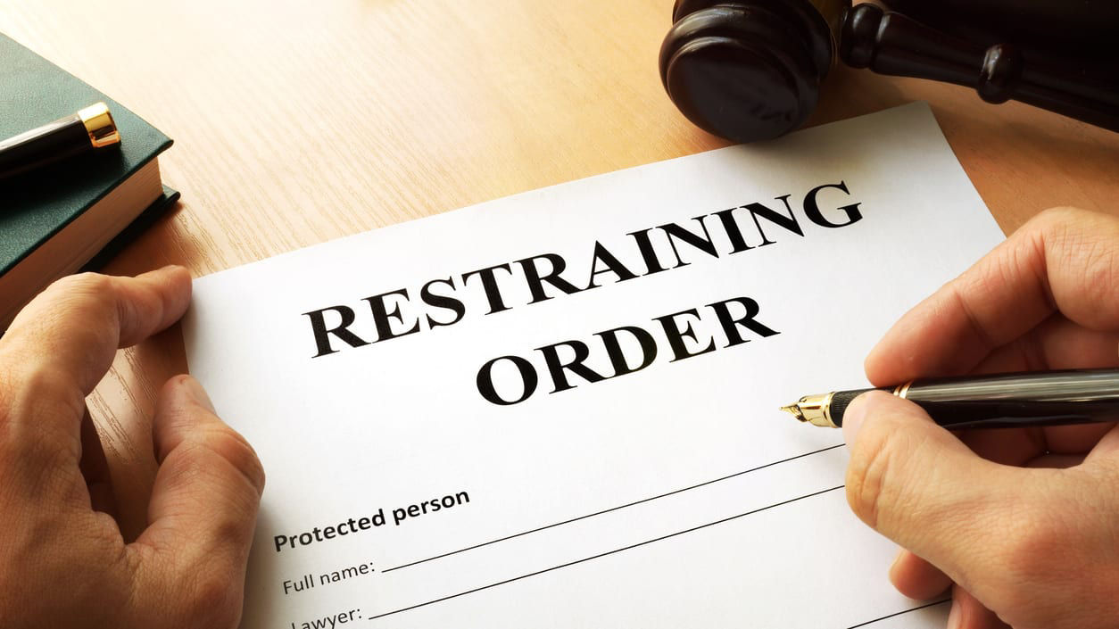 A hand writing a restraining order on a piece of paper.