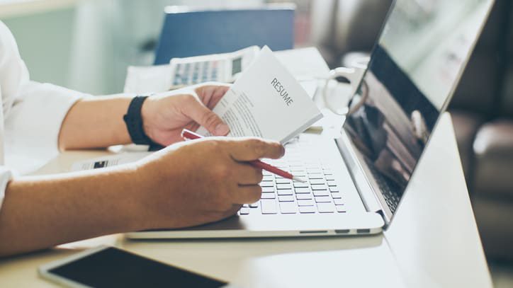 A man is working on a laptop with a paper in front of him.