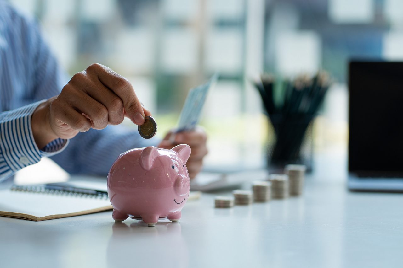 Hand putting coins into piggy bank and holding money