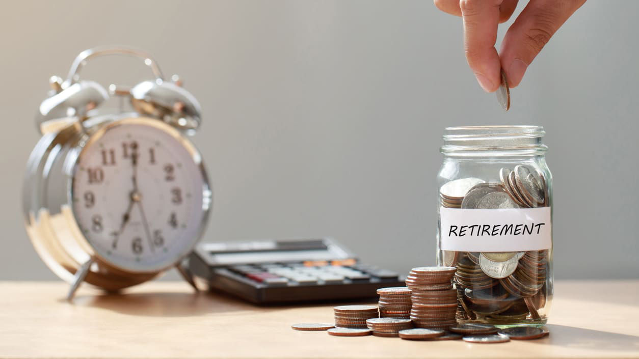 A hand is putting coins into a jar with an alarm clock.