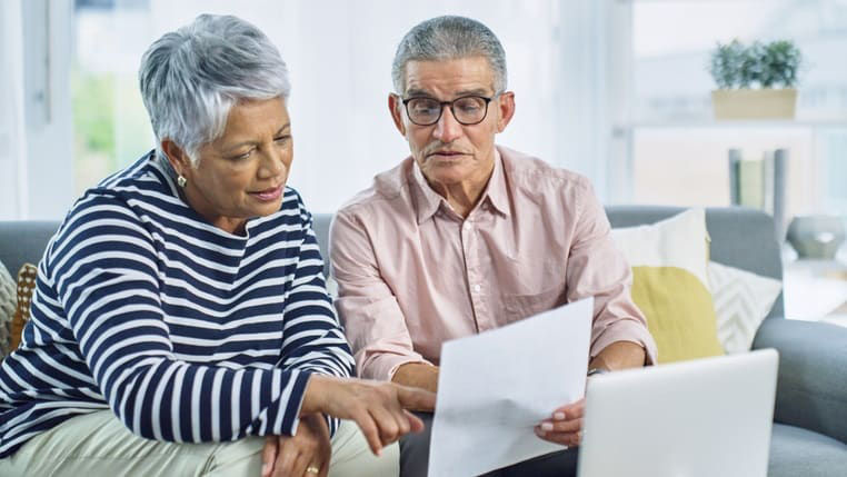 An older couple looking at a document on a laptop.