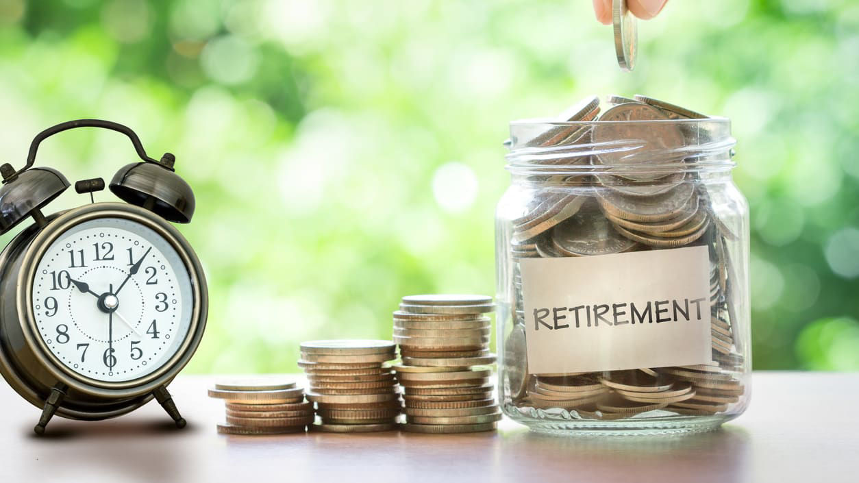A hand is putting coins into a jar with an alarm clock.