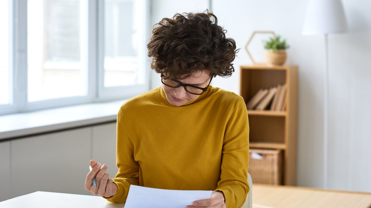 A woman is sitting at a table looking at paperwork.