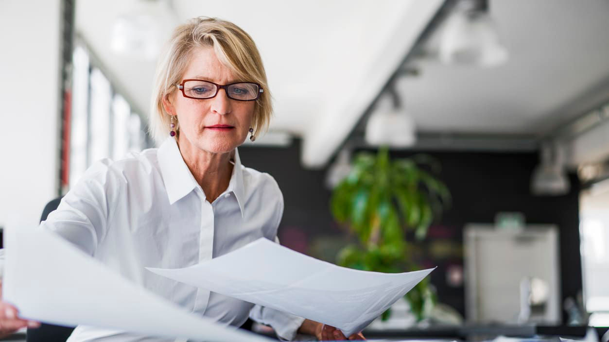 A woman in glasses is looking at a piece of paper.