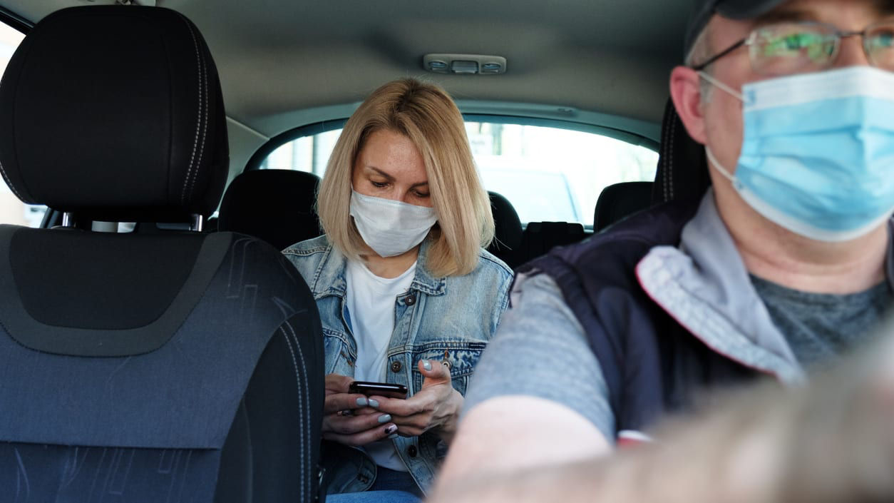 A man and woman wearing face masks in a car.