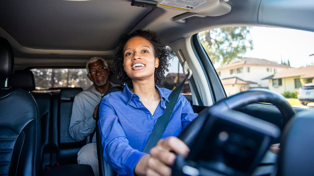 A woman driving a car with an older man in the driver's seat.