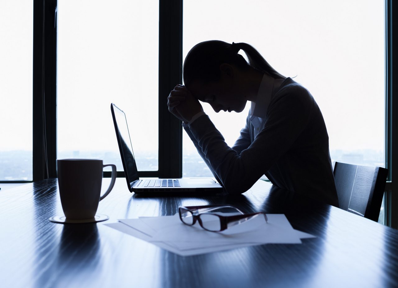 a woman balances her head on her hands in front of her computer at work