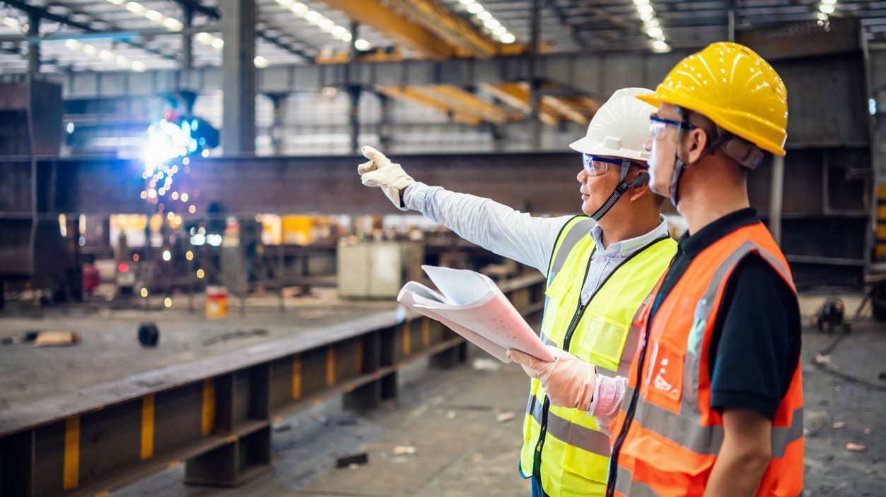 Two construction workers standing in a factory.