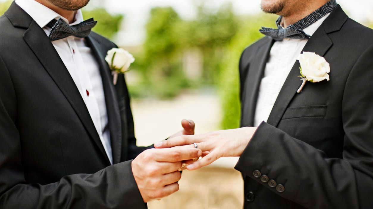 Two men in tuxedos putting their wedding rings on.
