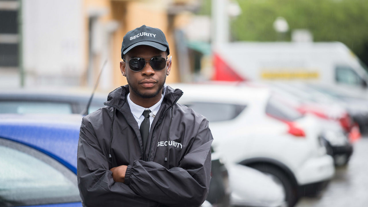 A man in a black jacket standing in front of parked cars.