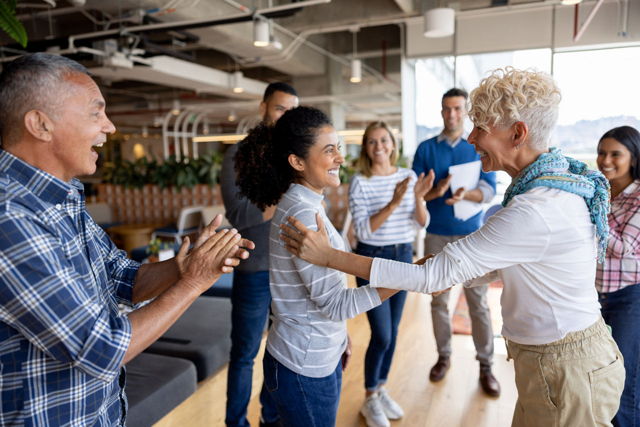 two women shaking hands surrounded by group of people clapping
