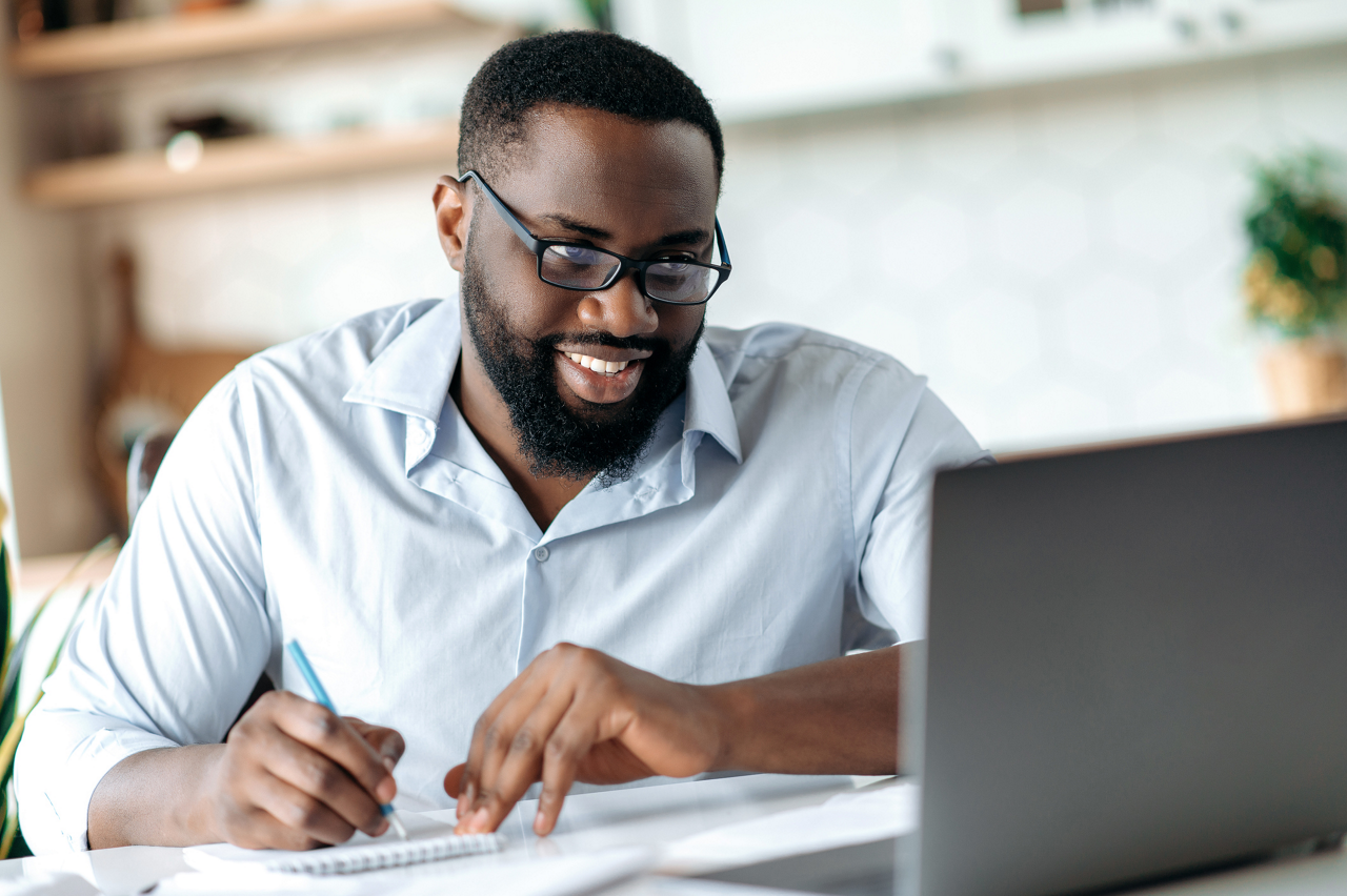 Friendly successful confident african american bearded male with glasses, broker, lawyer or manager working remotely, taking notes, talks by conference call with colleagues, distant learning, smiling