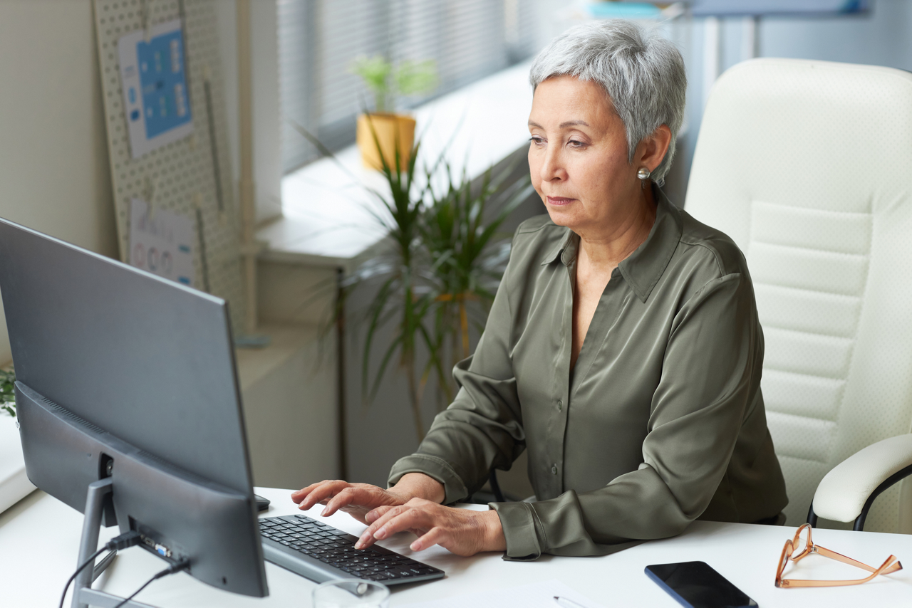 Portrait of senior female boss at workplace in office typing at computer keyboard