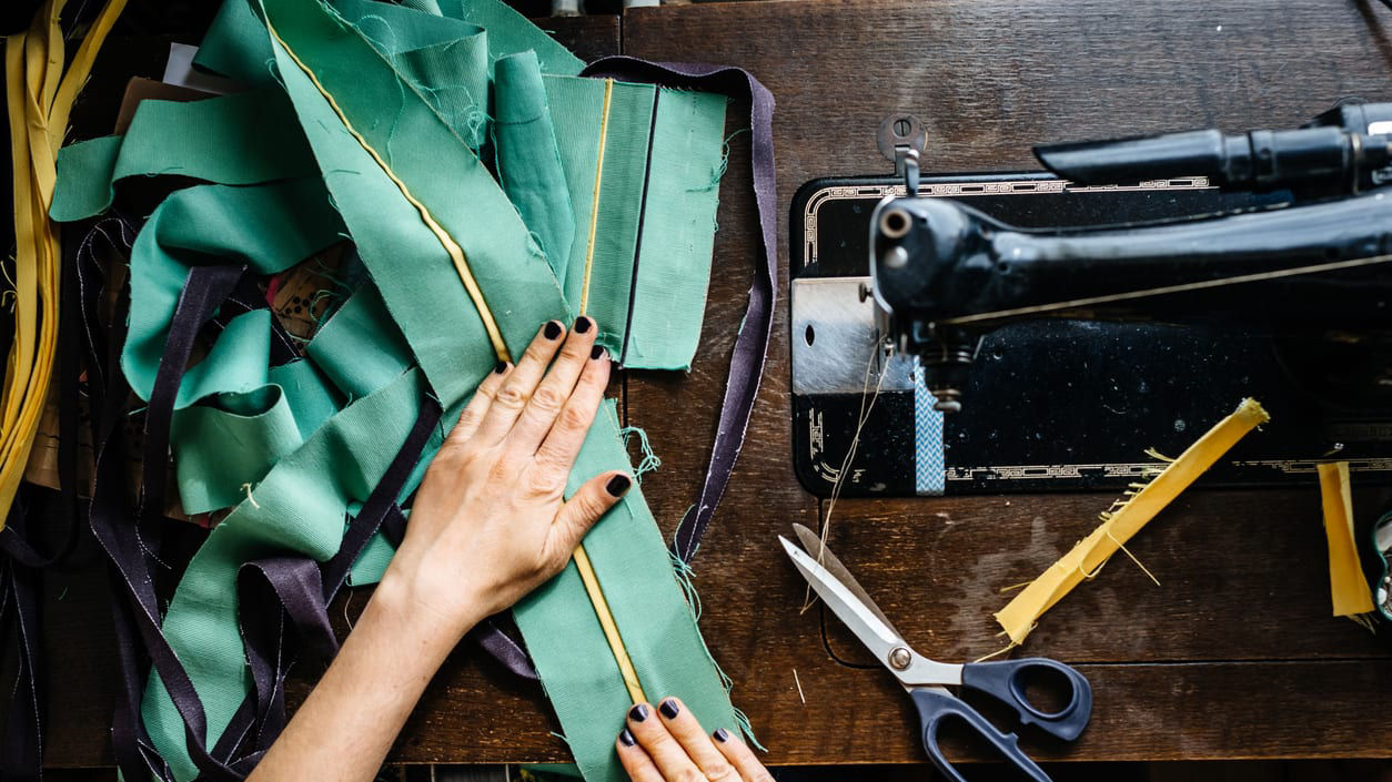 A woman is sewing green fabric on a sewing machine.