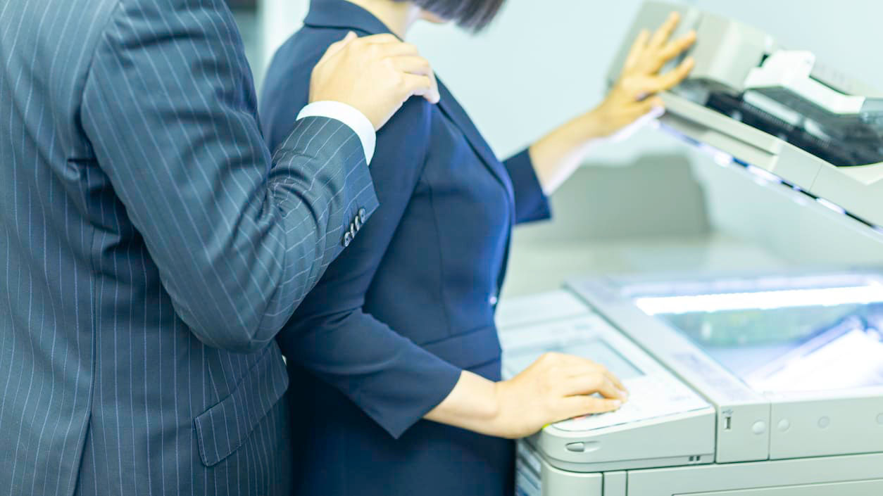 A man and woman standing next to a printer.