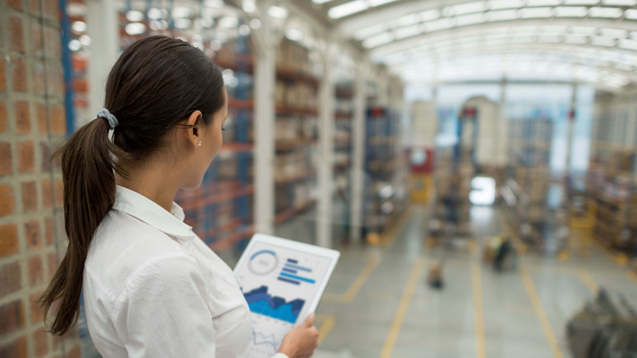 A woman is looking at a tablet in a warehouse.