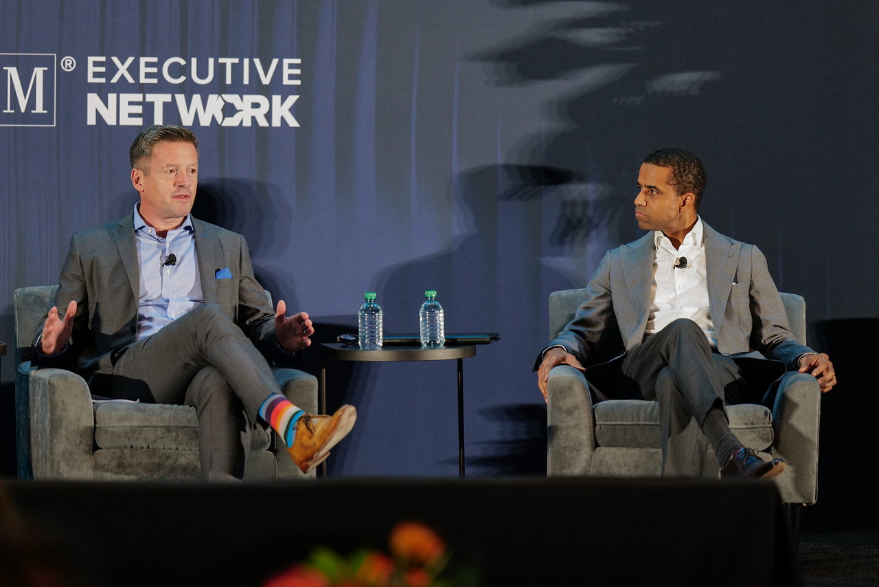 Adam Chamberlain sitting on stage at Visionaries Summit next to Lars Minns 