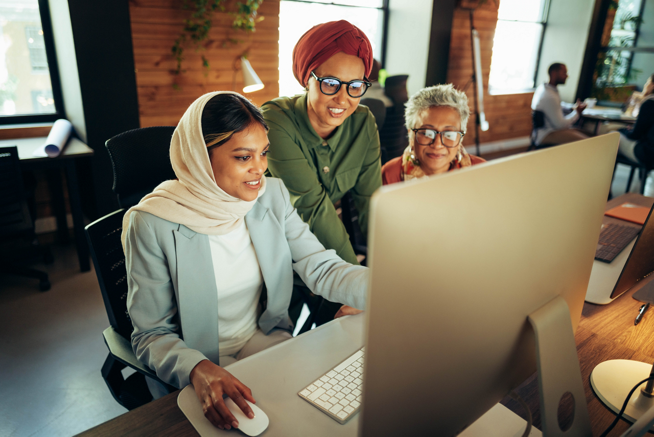 Three cheerful businesswomen having a discussion while looking at a computer screen in an office. Multicultural businesswomen working as a team in a modern co-working office.