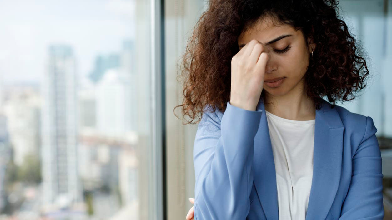 A woman is holding her head in her hands while looking out of a window.