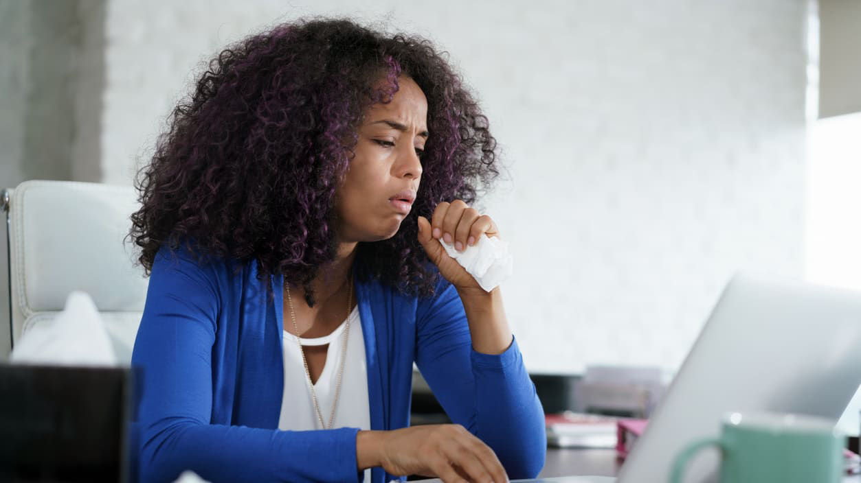 A woman is sitting at her desk with a tissue in her hand.