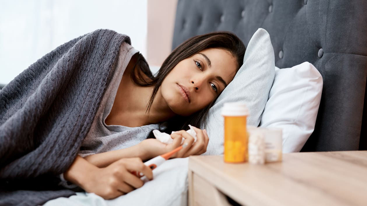 A woman laying in bed with a pill in her hand.