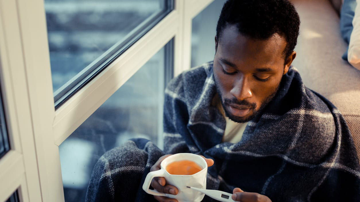 A man holding a cup of coffee while sitting in front of a window.