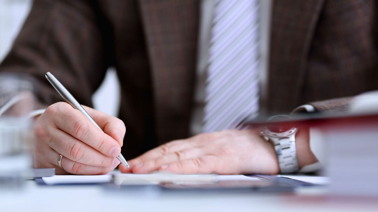 A man in a suit is writing on a piece of paper.