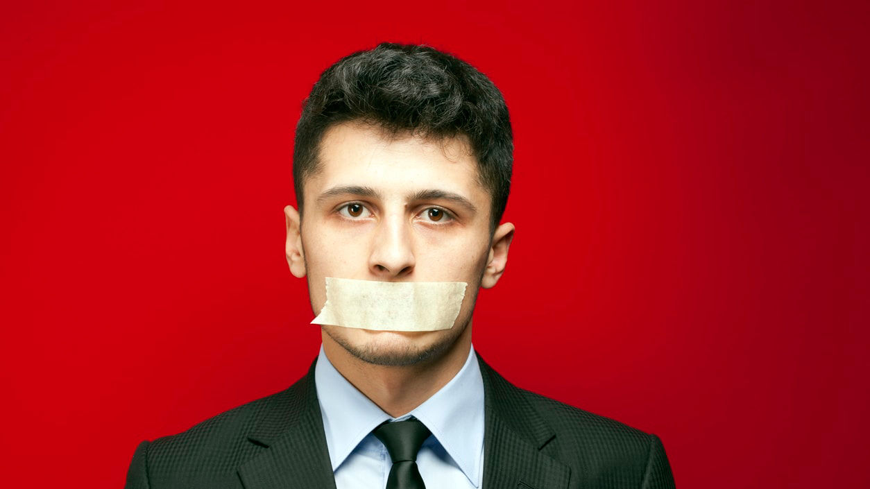 A man in a suit with a piece of tape on his mouth.