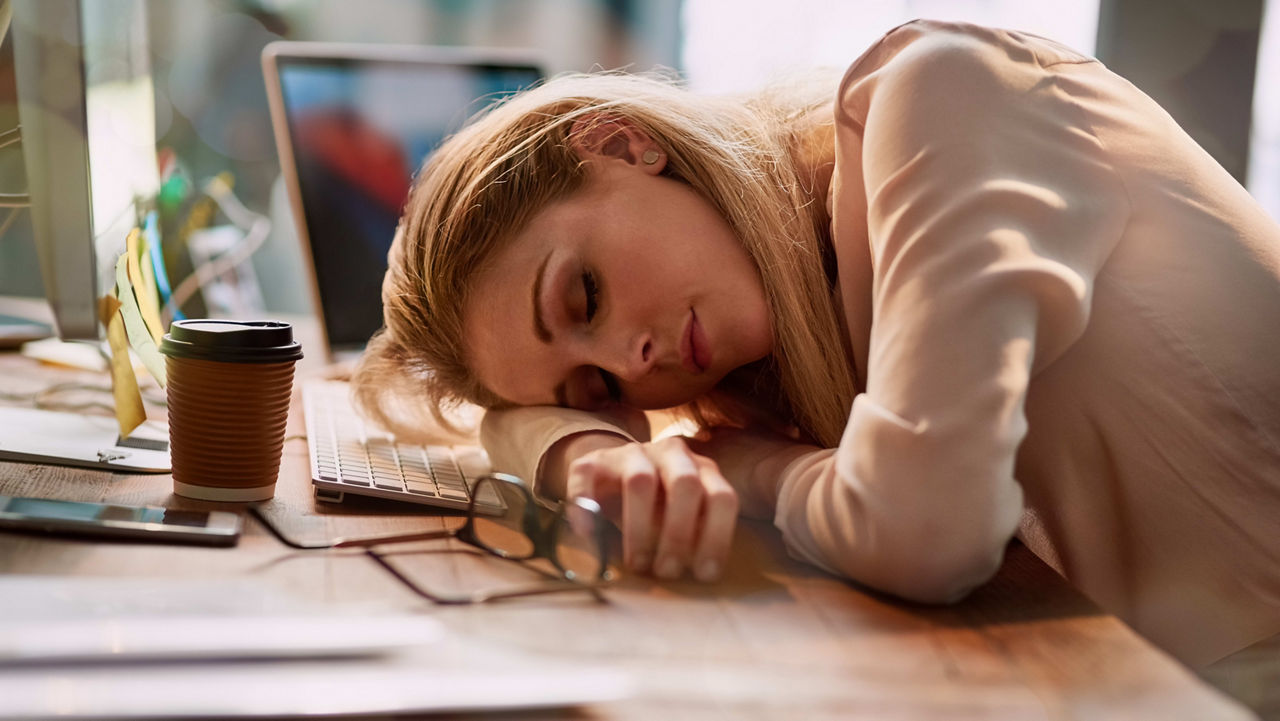 A woman is sleeping on a desk in front of a laptop.