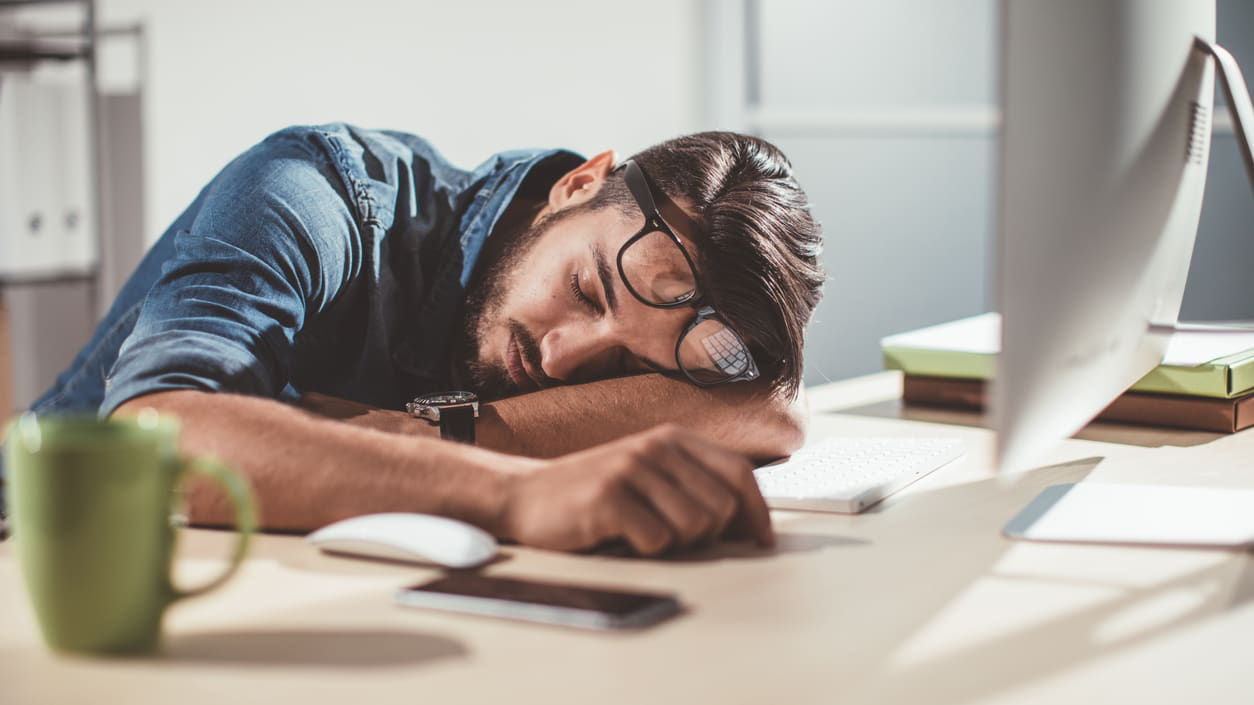 A man is sleeping on his desk at work.