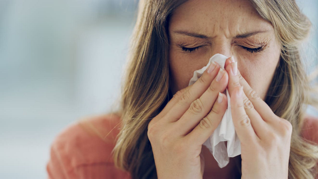 A woman blowing her nose with a tissue.