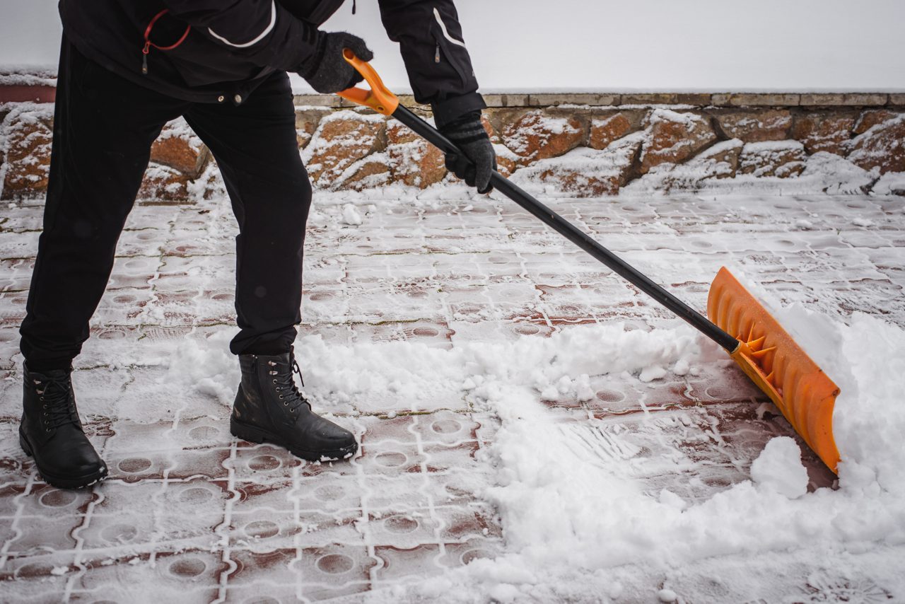 A person shovels snow from a brick sidewalk