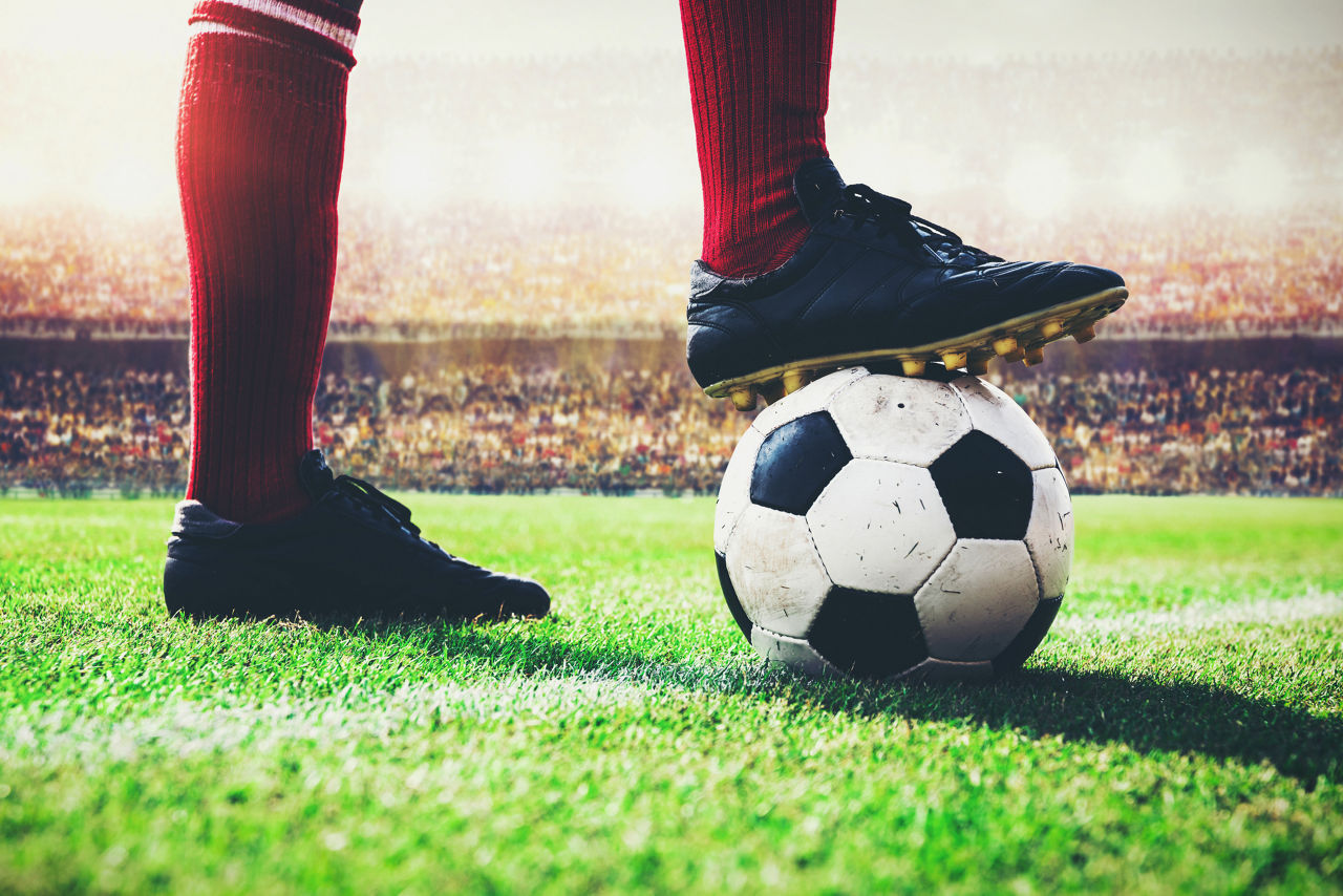 Someone with one foot on the turf of a soccer stadium, the other on a soccer ball.