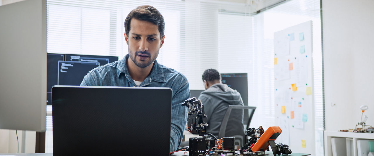 Black and white male software developer programmers work together on robot hand machine coding, use computer control robotic arm circuit. Programming language, hardware development technology concept