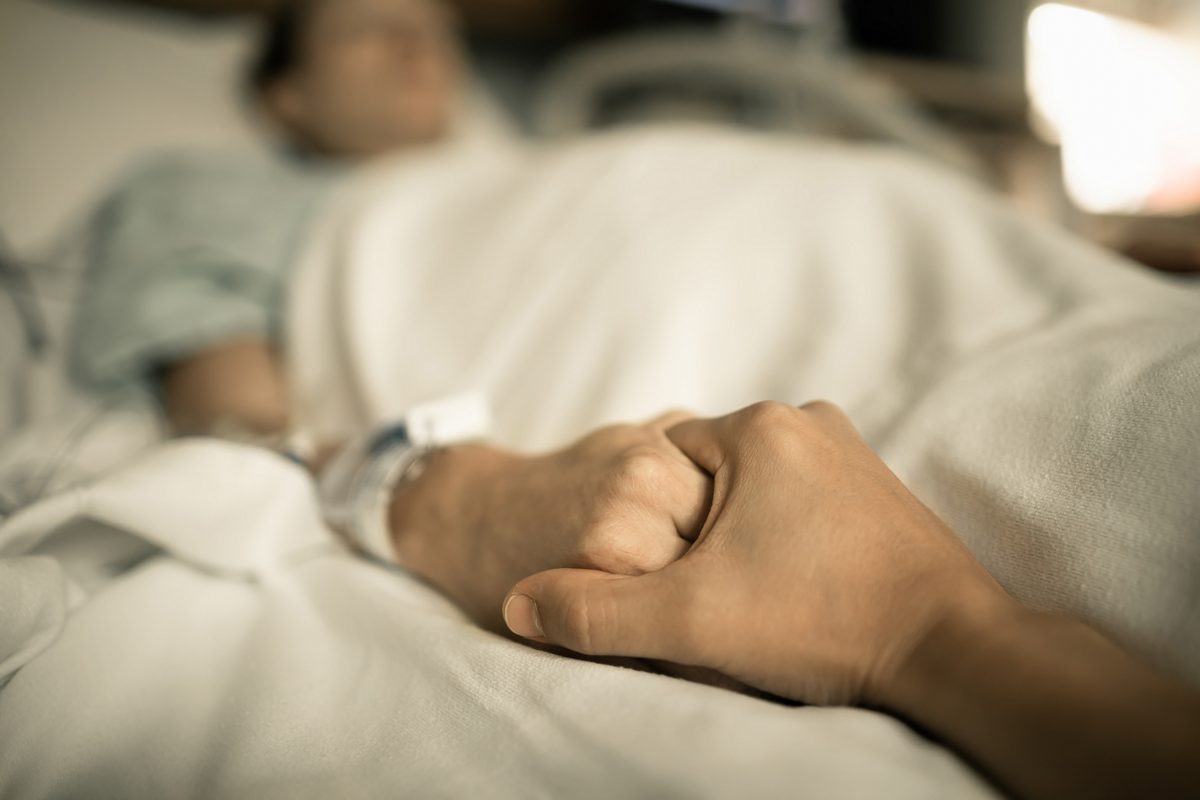 Someone holding the hand of someone who is ill and in bed.